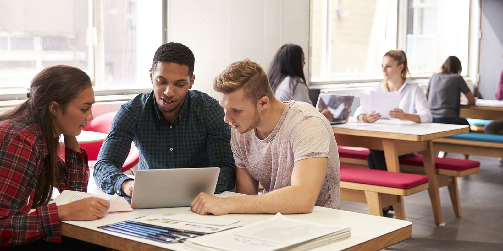 Group of students sitting around banched table, reviewing content on laptop screen.