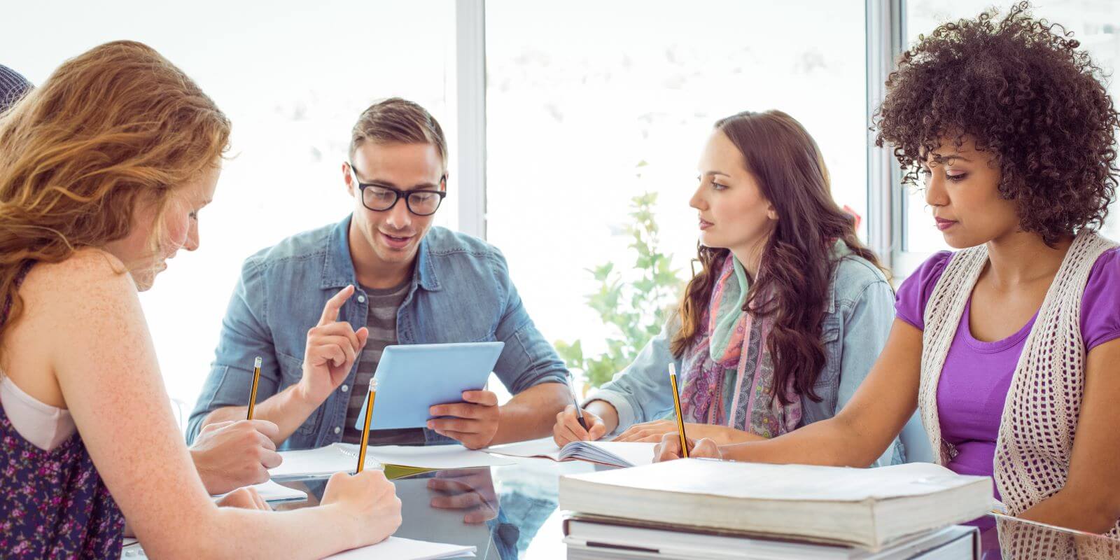 Group of individuals sitting around a conference table discussing content on a digital tablet.